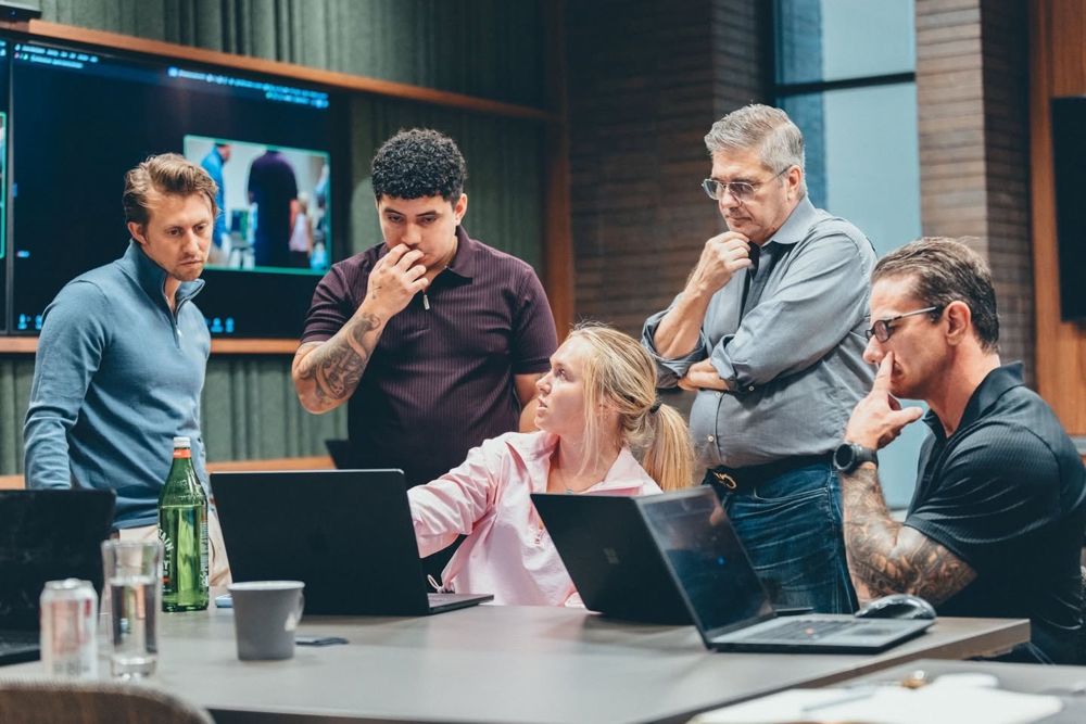 Ash pointing at a laptop while four other founders lean in around a conference table
