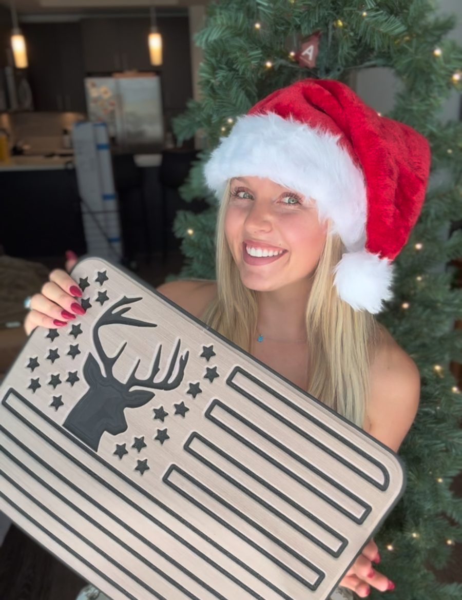 Ash in a Santa hat, smiling and holding a deer-and-flag boat decking pad from Decked Out Factory